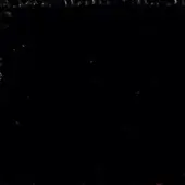 Dark abstract composition with granular texture at top and scattered bright particles, creating depth against a black background.